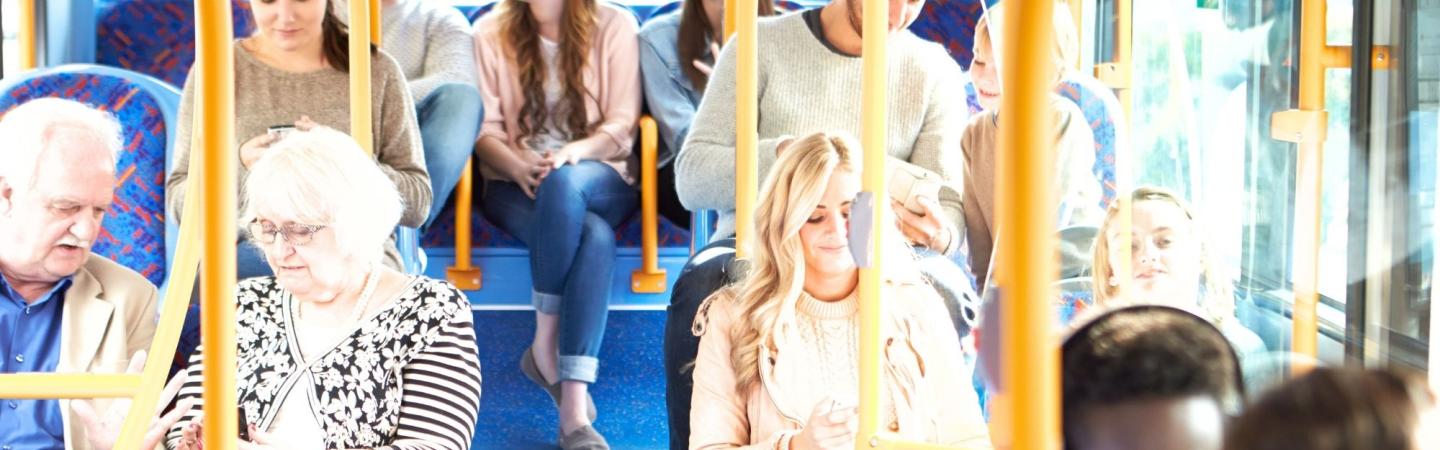 Image shows people on a London bus, it's a mixed crowd with people of all ages and races. 