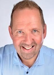 Alfie is smiling at the camera in a head and shoulders portrait. He has short brown hair, blue eyes and a blue shirt. 