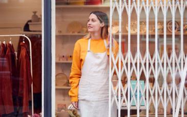 Image shows a woman shutting up her clothes shop